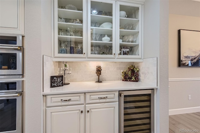 bar with tasteful backsplash, white cabinetry, light hardwood / wood-style floors, and wine cooler