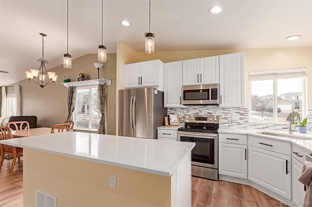 kitchen with a kitchen island, lofted ceiling, a sink, appliances with stainless steel finishes, and tasteful backsplash