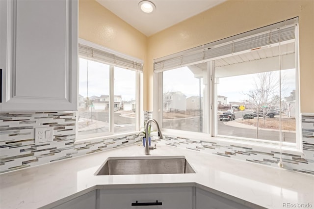 kitchen with backsplash, white cabinetry, light countertops, and a sink