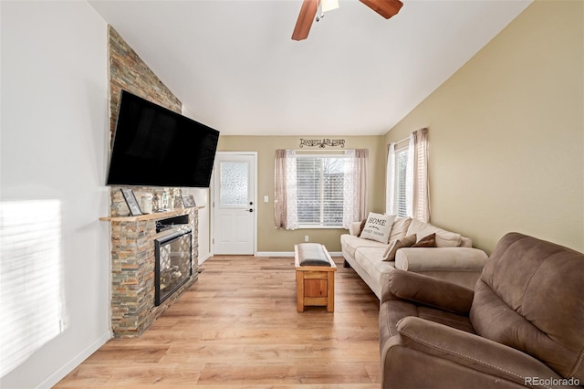 living area featuring vaulted ceiling, a fireplace, baseboards, and light wood finished floors