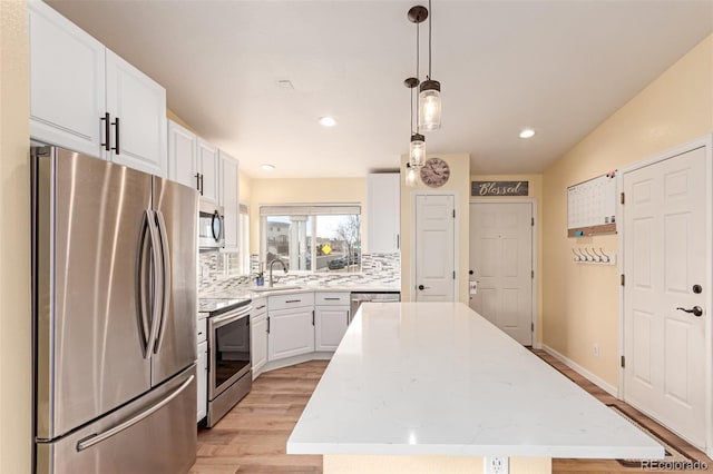 kitchen featuring stainless steel appliances, white cabinets, light wood-type flooring, backsplash, and a center island