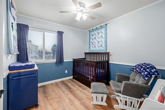 bedroom featuring a crib, crown molding, baseboards, light wood-style floors, and a ceiling fan