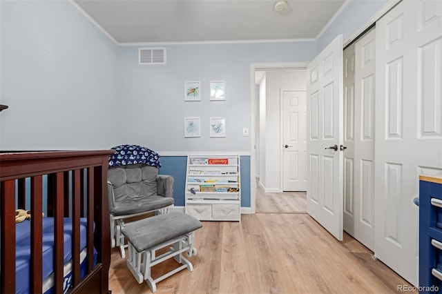 bedroom with baseboards, visible vents, ornamental molding, light wood-style floors, and a closet