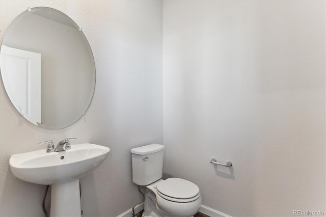 half bath featuring toilet, baseboards, and a sink