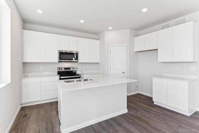 kitchen with dark wood-style floors, appliances with stainless steel finishes, white cabinetry, an island with sink, and baseboards