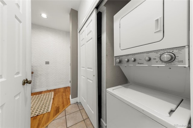 washroom featuring baseboards, stacked washer and dryer, laundry area, and light tile patterned flooring