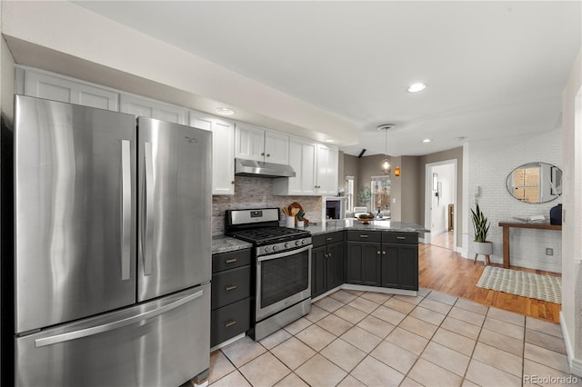 kitchen with light tile patterned floors, a peninsula, white cabinetry, under cabinet range hood, and stainless steel appliances