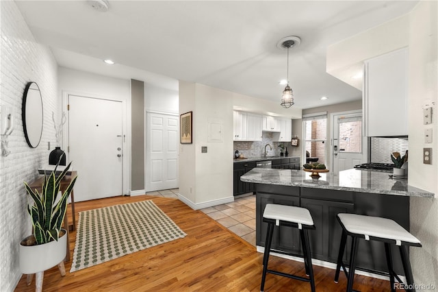 kitchen featuring a peninsula, light wood-style flooring, white cabinetry, decorative backsplash, and a sink