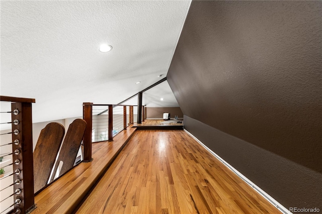 bonus room with baseboards, light wood finished floors, a textured ceiling, and vaulted ceiling
