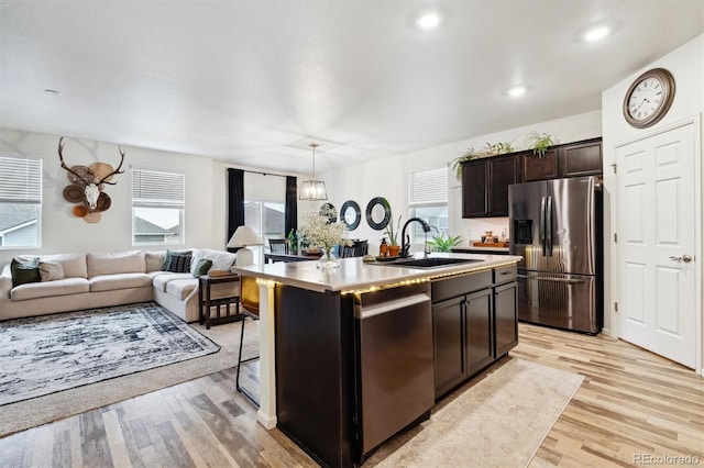 kitchen with dark brown cabinetry, a sink, open floor plan, appliances with stainless steel finishes, and light wood finished floors