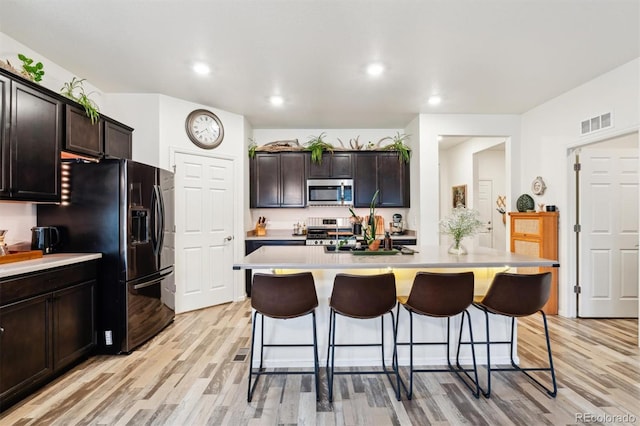 kitchen featuring visible vents, stainless steel microwave, stove, black refrigerator with ice dispenser, and light countertops