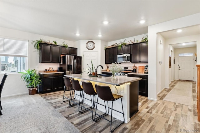 kitchen with a center island with sink, appliances with stainless steel finishes, dark brown cabinets, a kitchen bar, and a sink