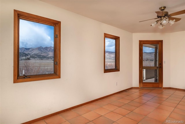 empty room with ceiling fan, light tile patterned flooring, a mountain view, and baseboards