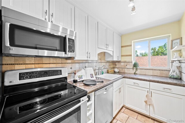 2047 S Milwaukee St Unit 4, Denver, CO 80210 - kitchen featuring decorative backsplash, appliances with stainless steel finishes, a sink, white cabinetry, and stone tile floors