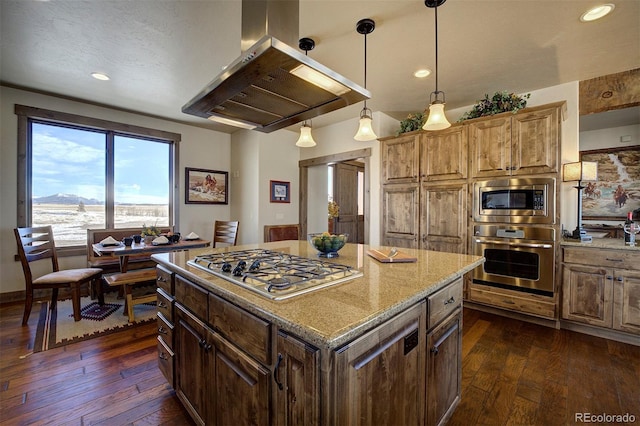 kitchen with appliances with stainless steel finishes, a center island, island exhaust hood, hanging light fixtures, and light stone counters