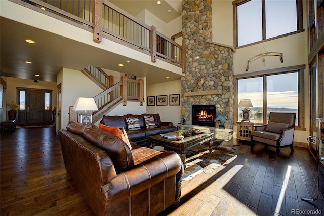 living room featuring a towering ceiling, hardwood / wood-style floors, and a stone fireplace