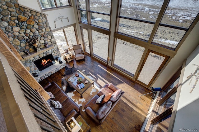 living room with dark wood-type flooring, a towering ceiling, and a stone fireplace