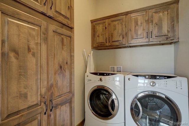 clothes washing area with washing machine and clothes dryer and cabinets