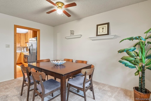 dining space featuring a textured ceiling, ceiling fan, and light carpet