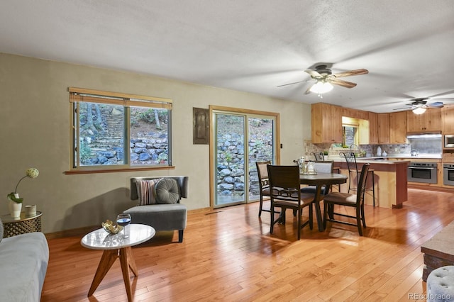 dining space with light wood-type flooring, plenty of natural light, a textured ceiling, and ceiling fan