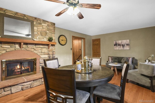 dining room with a ceiling fan, wood finished floors, and a fireplace