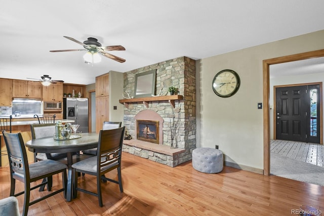 dining space featuring light wood-type flooring, baseboards, a ceiling fan, and a fireplace