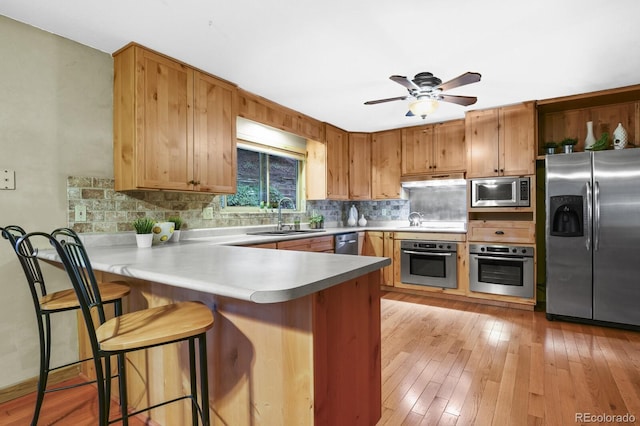 kitchen with light wood-type flooring, decorative backsplash, appliances with stainless steel finishes, a peninsula, and a sink