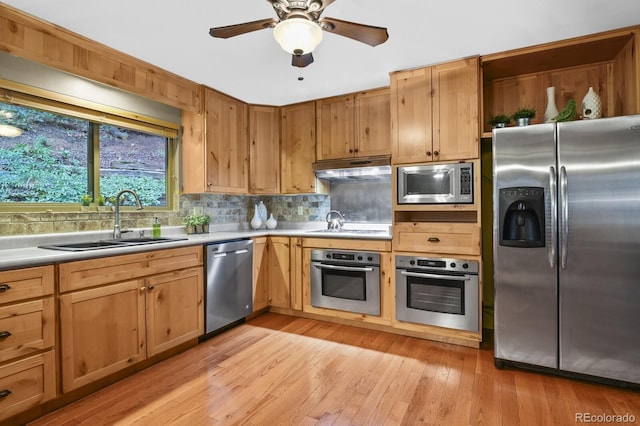 kitchen featuring under cabinet range hood, light countertops, decorative backsplash, stainless steel appliances, and a sink