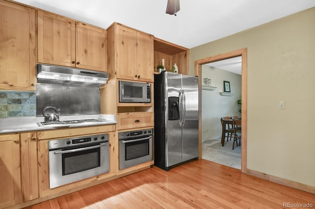 kitchen featuring light wood-type flooring, light countertops, under cabinet range hood, appliances with stainless steel finishes, and tasteful backsplash