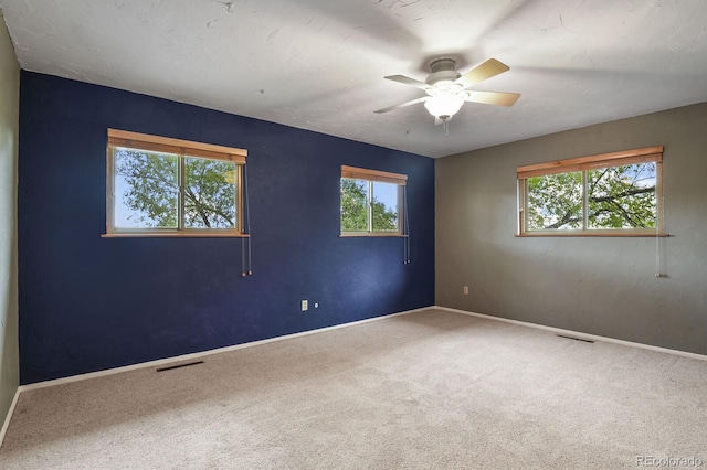 carpeted spare room with visible vents, a ceiling fan, and baseboards