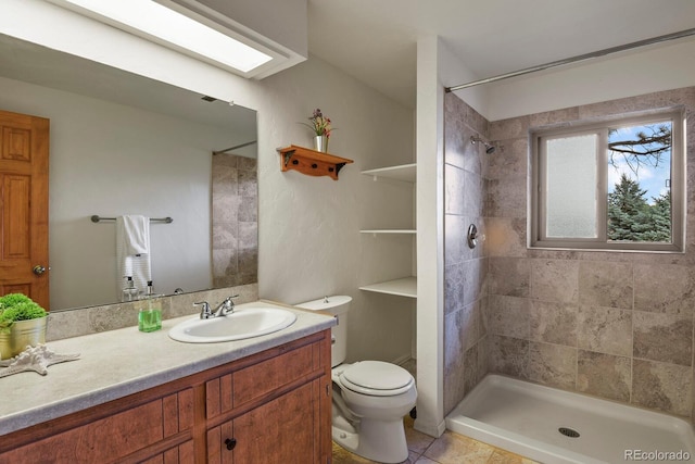 bathroom with toilet, a tile shower, a skylight, tile patterned flooring, and vanity