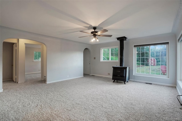 carpeted spare room featuring ceiling fan and a wood stove