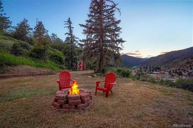 yard at dusk featuring an outdoor fire pit, a mountain view, and a storage unit