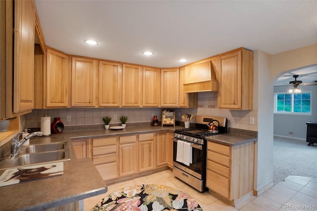 kitchen featuring premium range hood, sink, light colored carpet, stainless steel gas range oven, and light brown cabinets