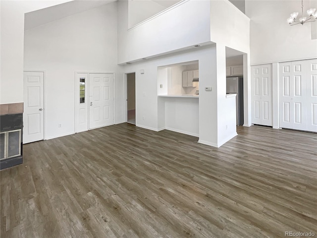 unfurnished living room with a towering ceiling, dark wood-style floors, a chandelier, and baseboards