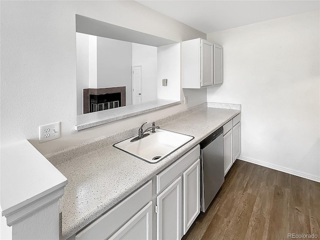 kitchen featuring stainless steel dishwasher, a sink, light countertops, dark wood-type flooring, and a multi sided fireplace