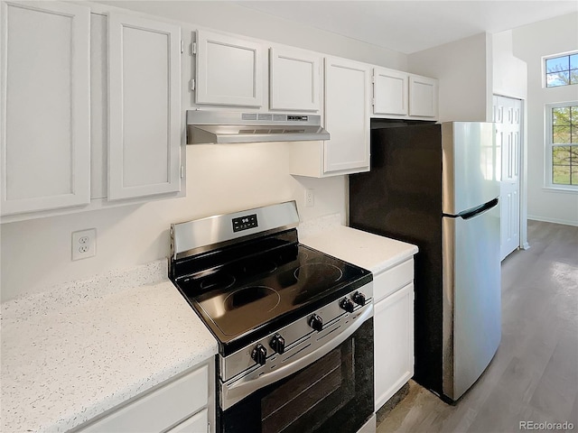kitchen featuring under cabinet range hood, appliances with stainless steel finishes, white cabinets, wood finished floors, and light stone counters