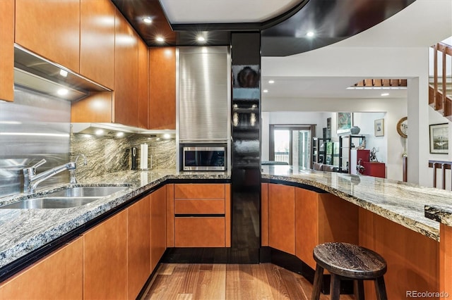 kitchen with a sink, stone counters, tasteful backsplash, and stainless steel microwave