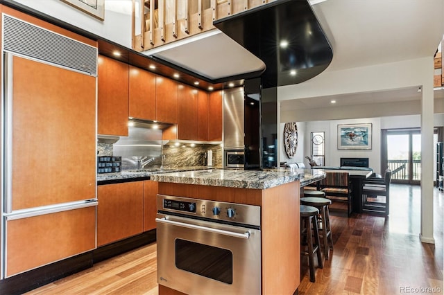 kitchen with a breakfast bar, wood finished floors, paneled fridge, and stainless steel oven