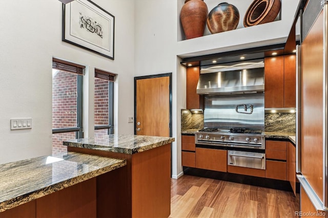 kitchen with brown cabinetry, backsplash, a warming drawer, and wood finished floors