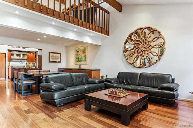 living area with baseboards, beam ceiling, light wood-style flooring, and a towering ceiling