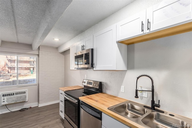 kitchen featuring white cabinetry, sink, stainless steel appliances, a wall mounted air conditioner, and wood counters