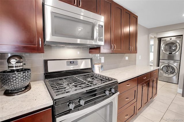 kitchen with light tile patterned flooring, stacked washer / drying machine, tasteful backsplash, light stone counters, and appliances with stainless steel finishes