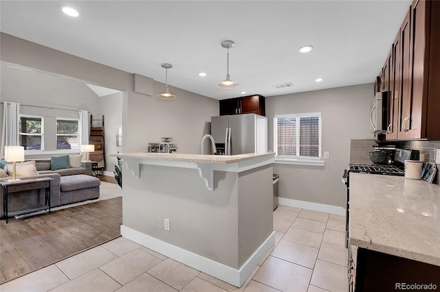 kitchen with light tile patterned flooring, light stone counters, a kitchen breakfast bar, pendant lighting, and stainless steel appliances