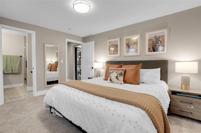 bedroom with light carpet, ensuite bathroom, and stacked washing maching and dryer