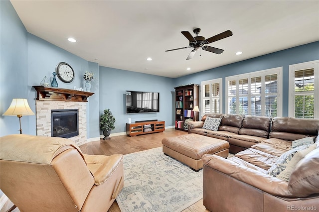 living room with a stone fireplace, light wood-type flooring, and ceiling fan