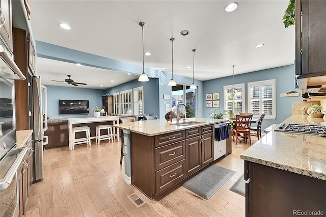 kitchen featuring light hardwood / wood-style floors, sink, a kitchen island with sink, light stone countertops, and decorative light fixtures