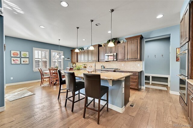 kitchen featuring a center island with sink, stainless steel appliances, light wood-type flooring, pendant lighting, and a kitchen breakfast bar