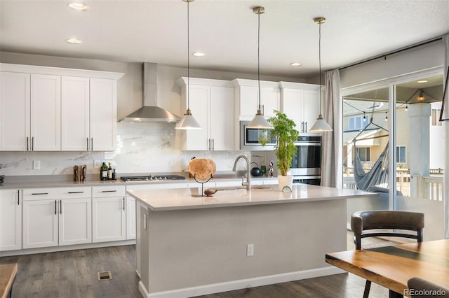 kitchen featuring a center island with sink, white cabinetry, wall chimney range hood, dark hardwood / wood-style flooring, and hanging light fixtures