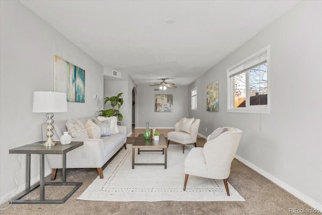 carpeted living area with arched walkways, ceiling fan, visible vents, and baseboards